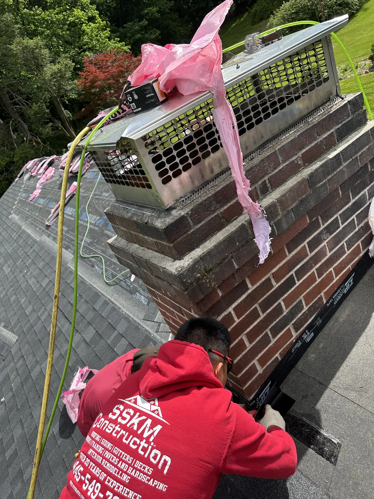 SSKM crew member installing flashing around a brick chimney on a shingle roof