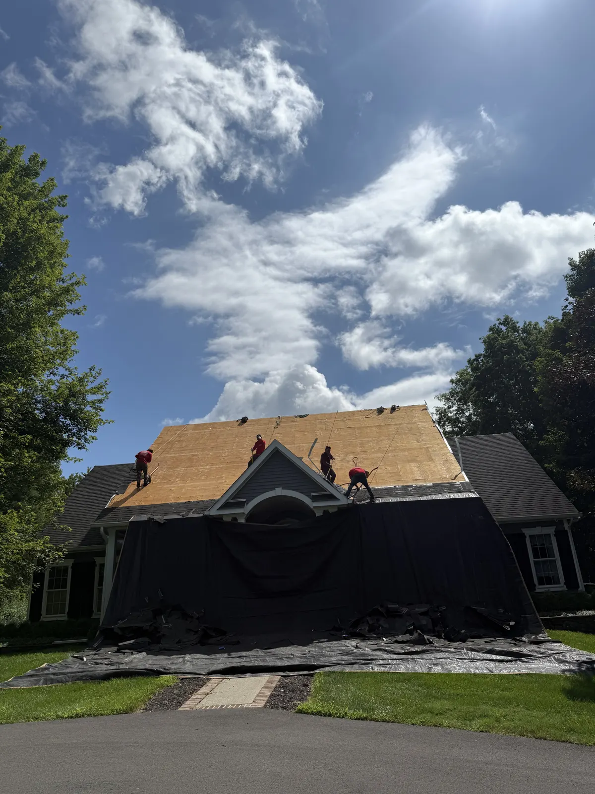 Crew installing new roof decking with the lower roof protected by a tarp