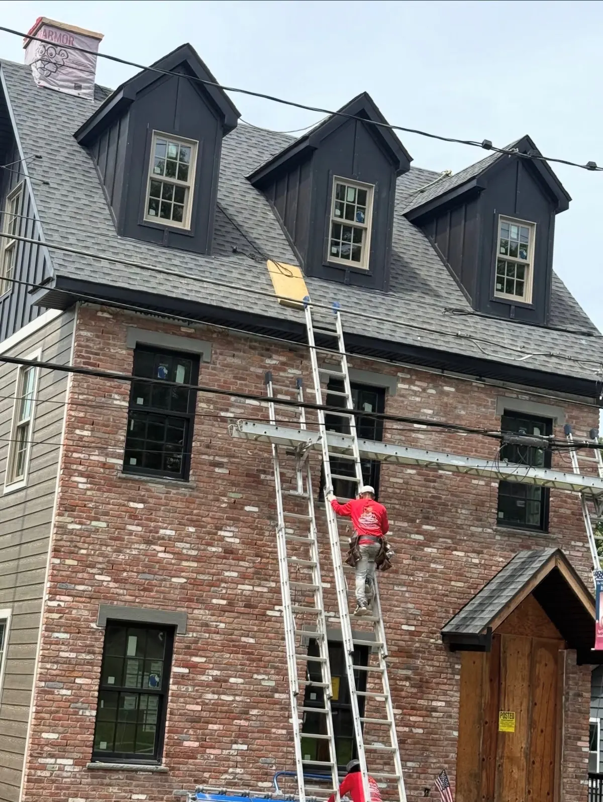 SSKM crew member climbing a ladder to the new shingle roof on a brick home with three dormers