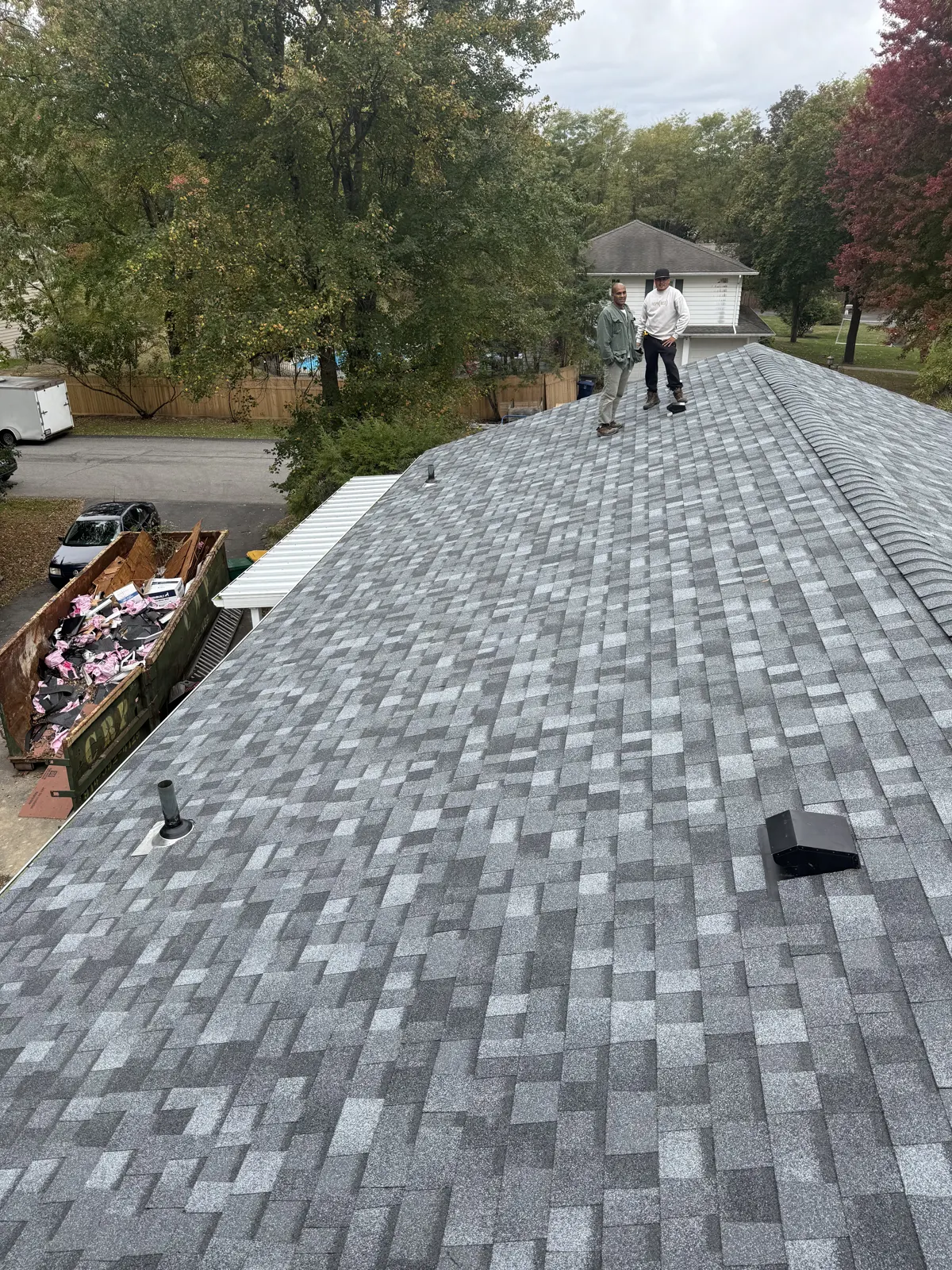 Finished gray shingle roof with a debris dumpster staged in the driveway