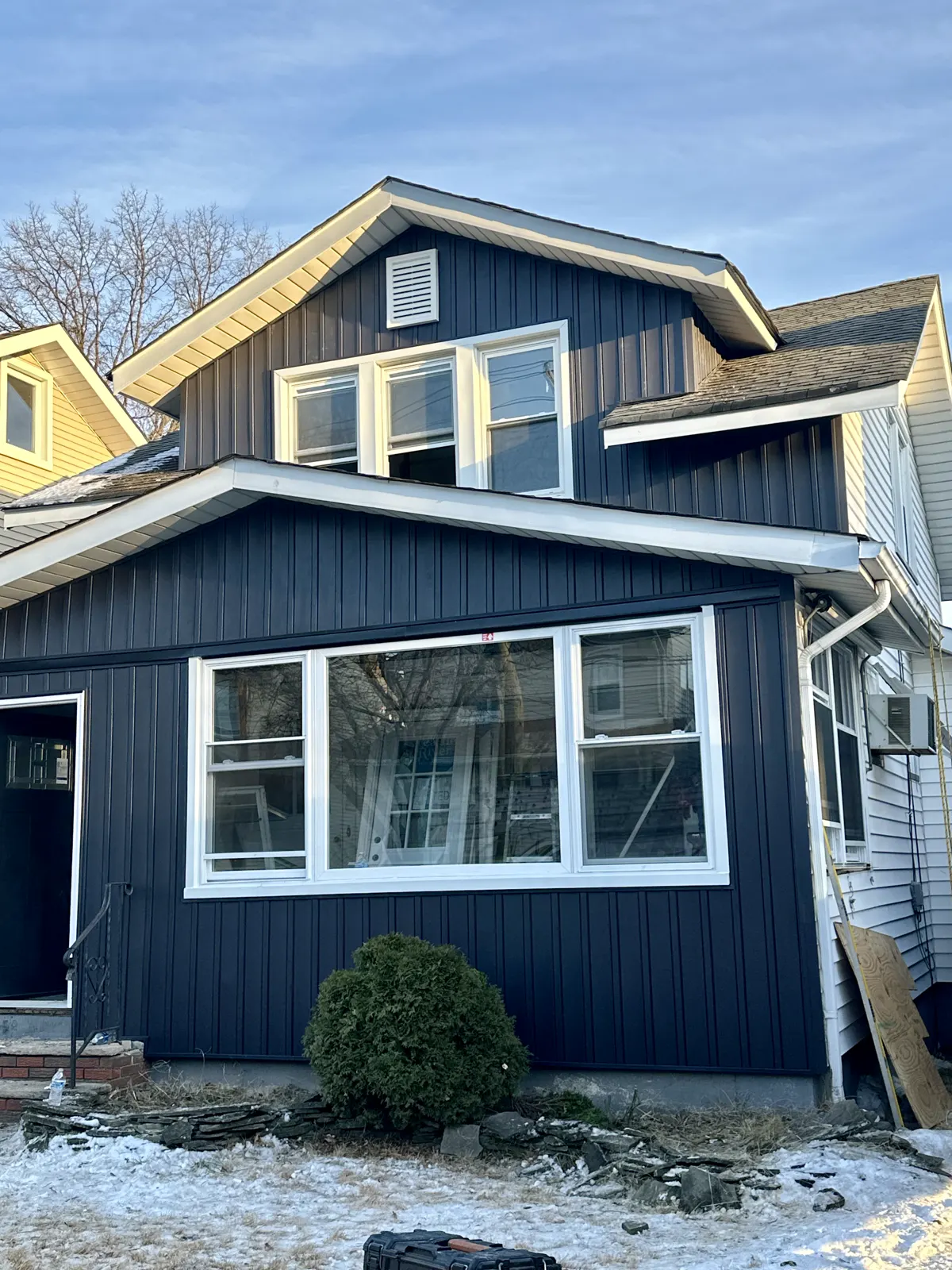 Finished navy blue siding with white trim on a home with a bay window