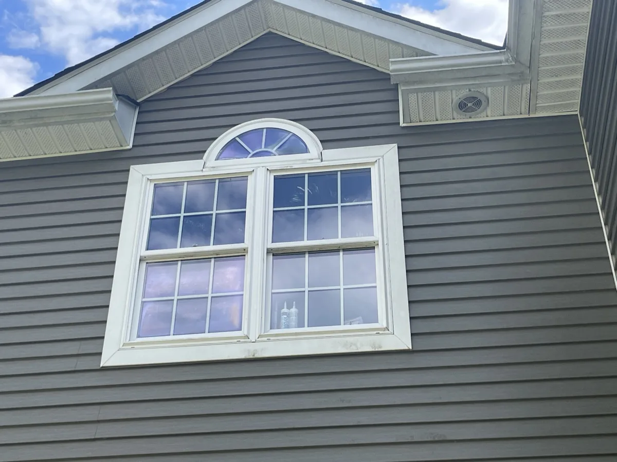 Finished replacement window with an arched transom on gray siding