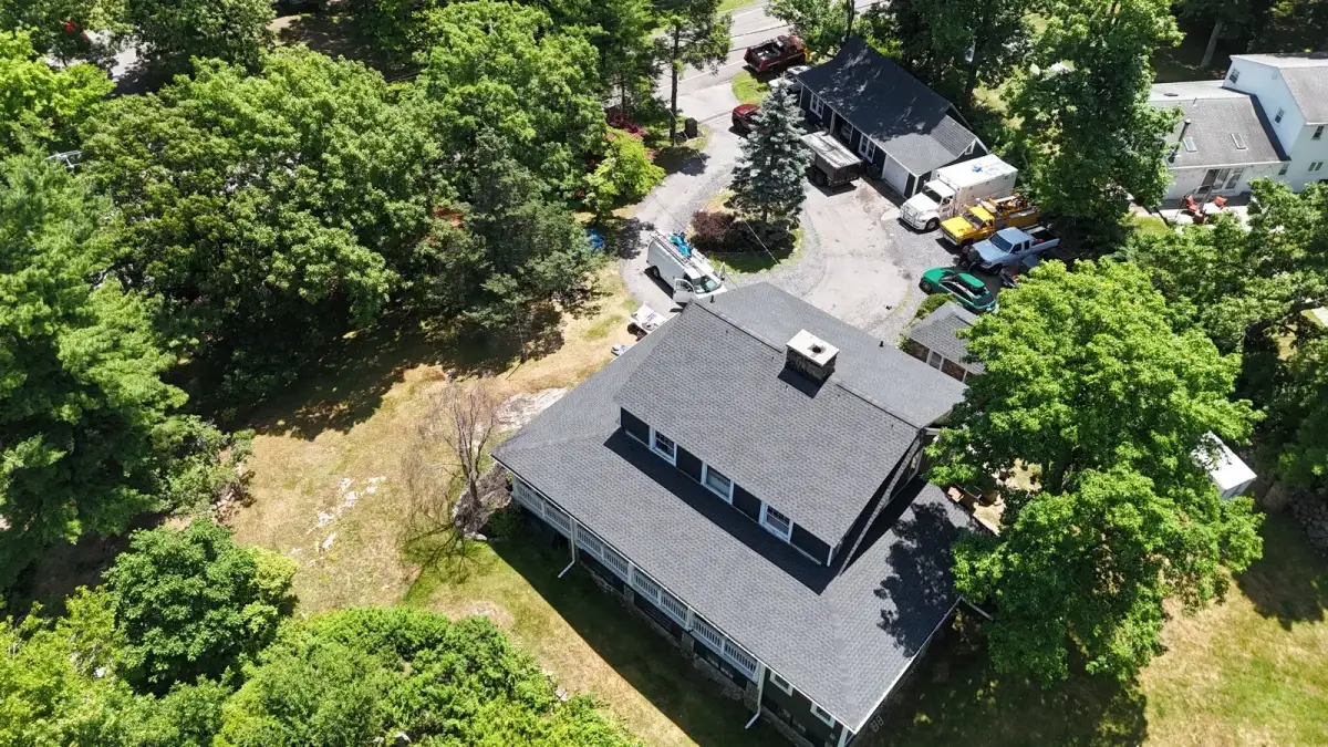 Aerial view of a finished gray shingle roof with SSKM Construction crew vehicles staged in the driveway in Monroe, NY
