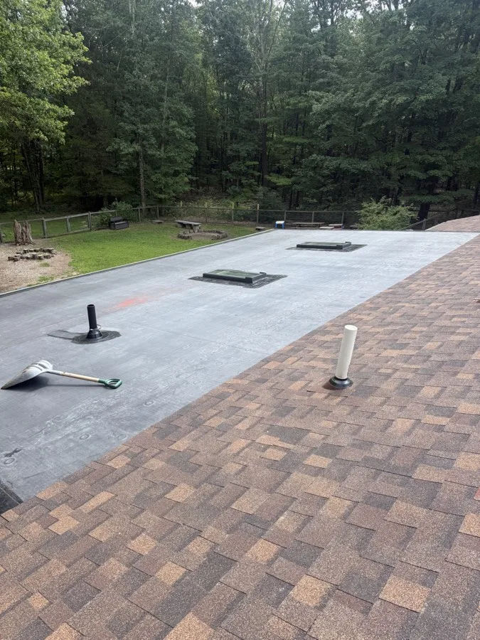 Flat roof section with two new skylights adjoining a shingle roof