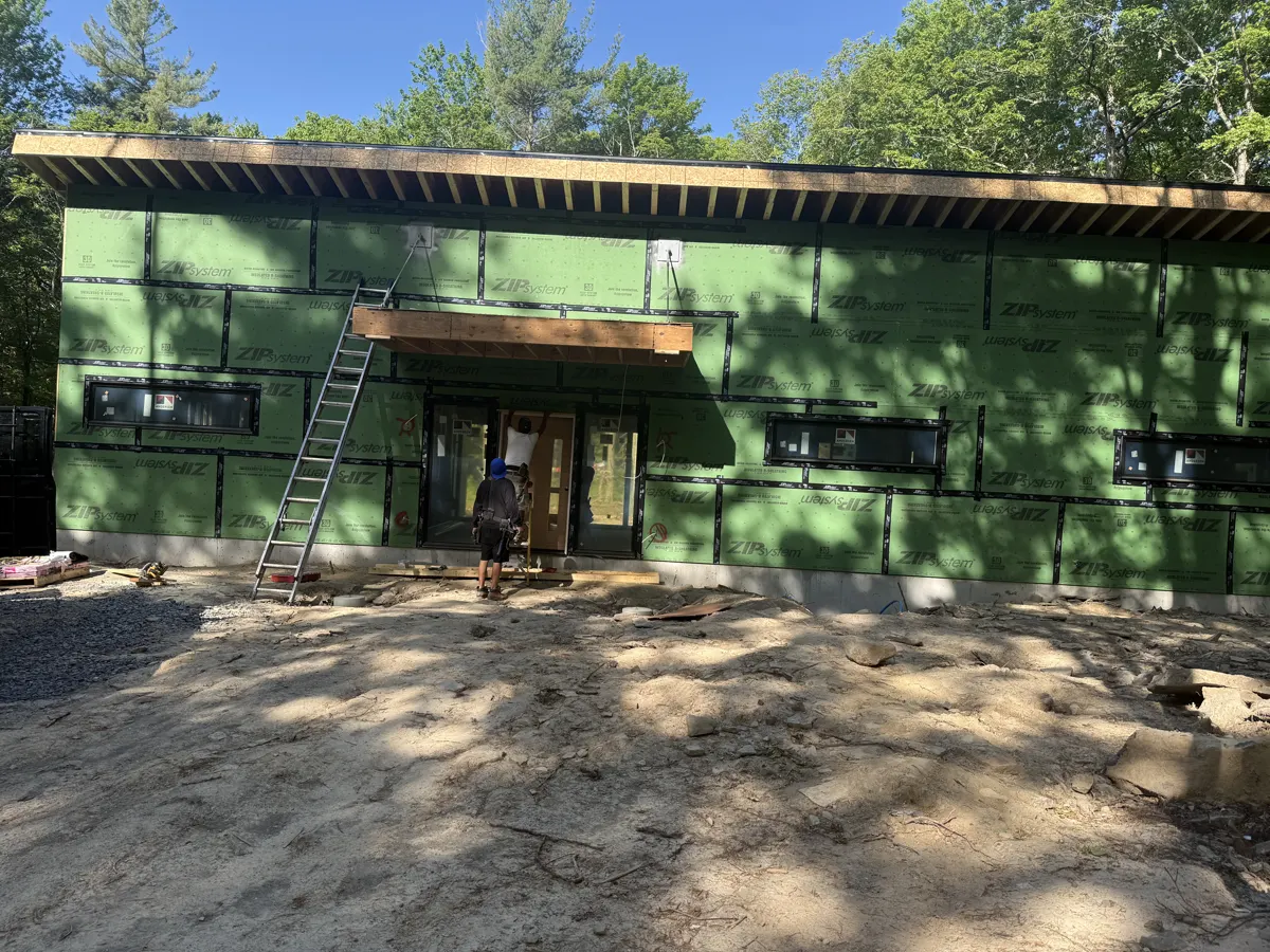 New construction home wrapped in green sheathing with a covered entry