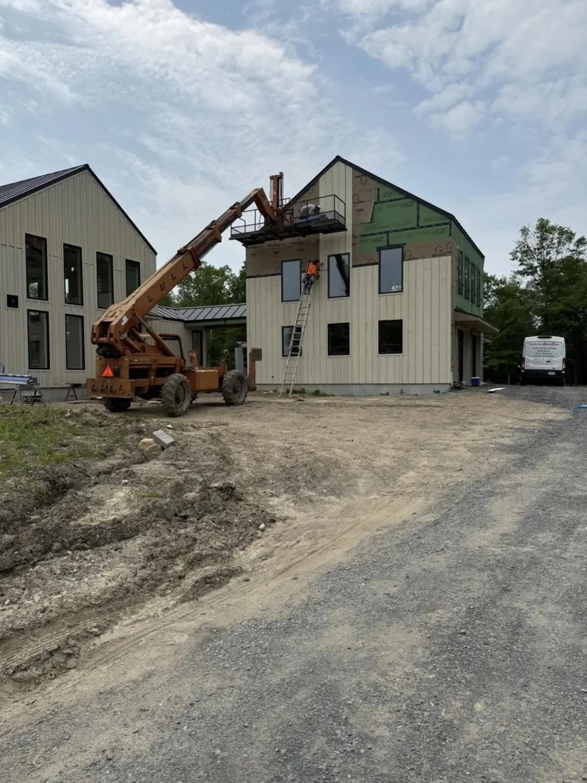 Telehandler lift assisting siding installation on a two-story new construction home