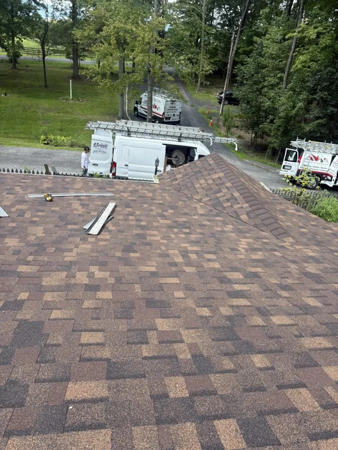 New shingle roof ridge line, with SSKM Construction crew vehicles staged in the driveway below
