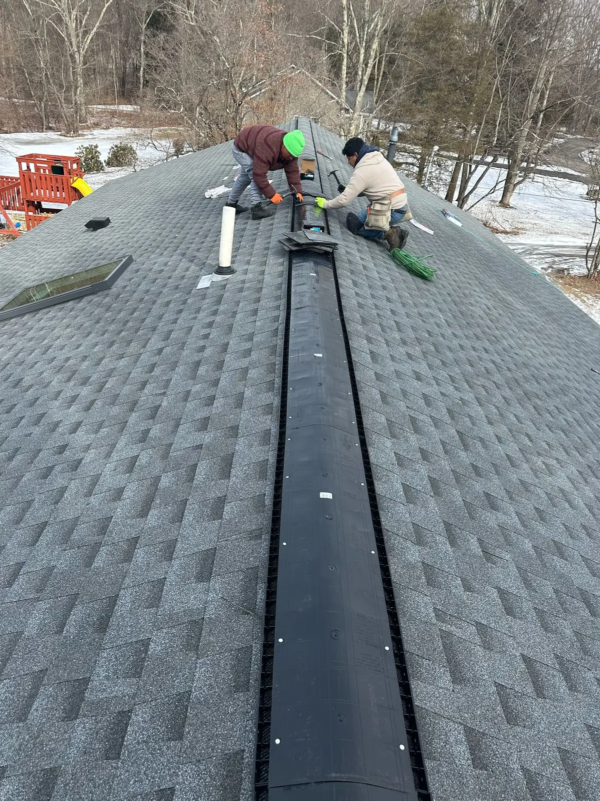 Crew installing ridge vent material near a skylight on a shingle roof