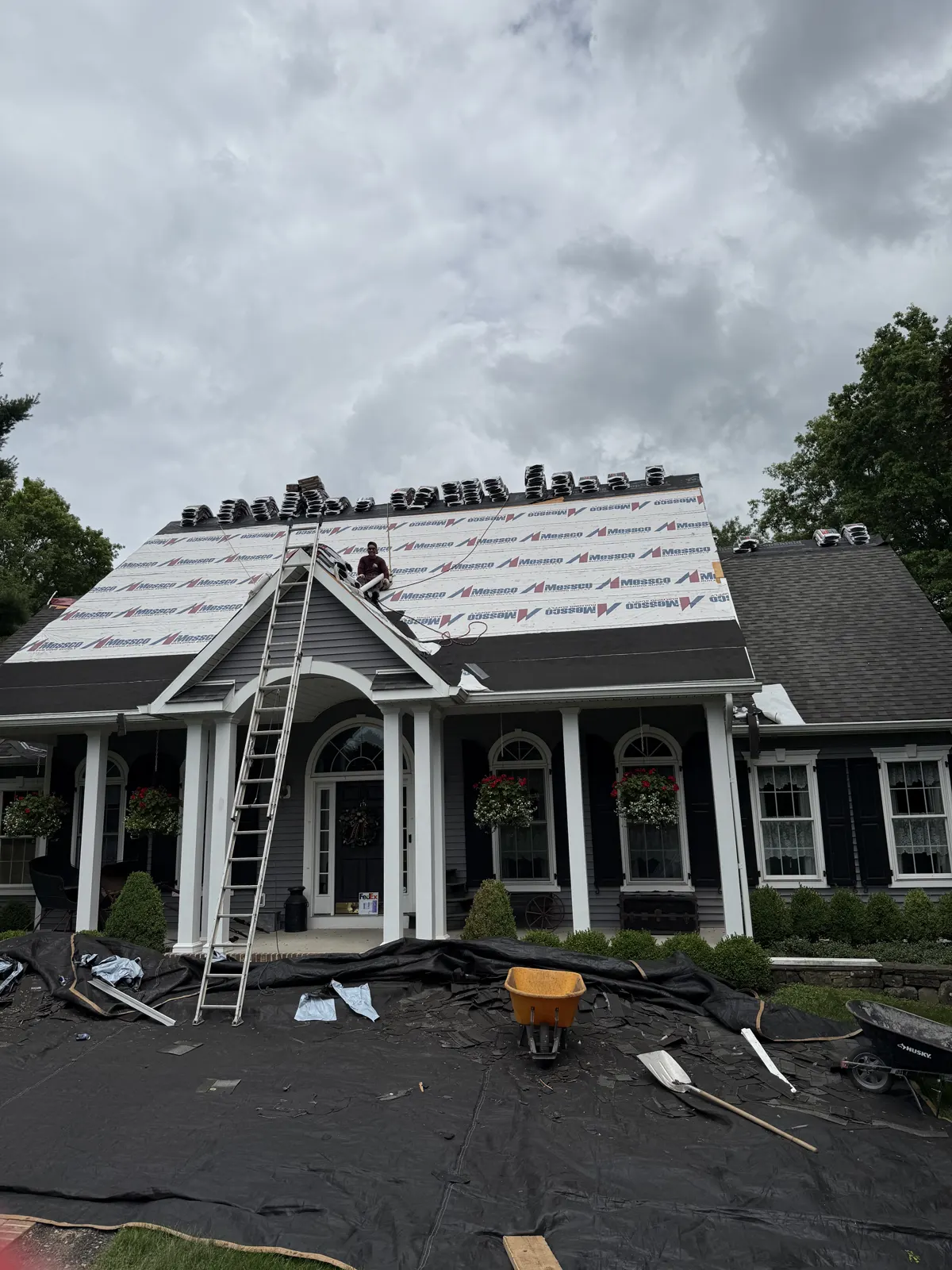 Roof underlayment going on a home with a front portico and a crew member on a ladder