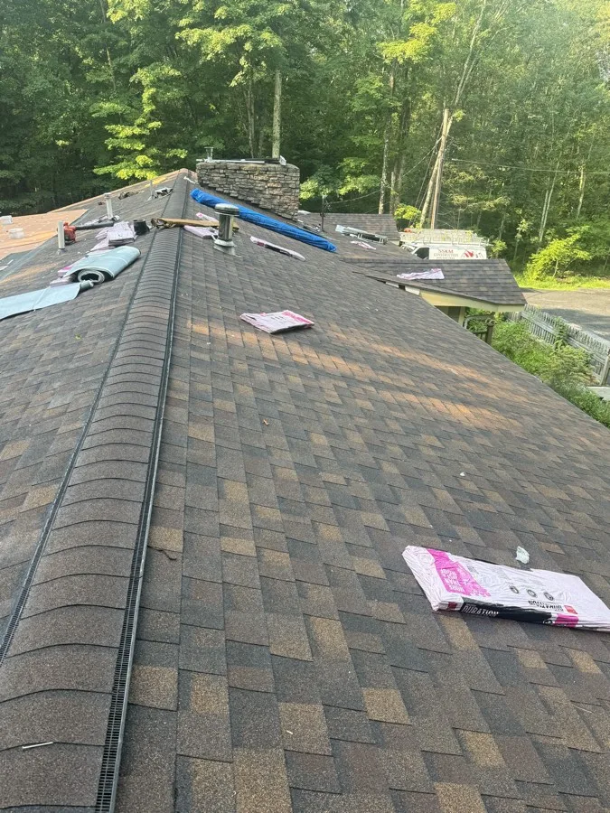 Roofing crew wrapping up ridge work in early morning light, with shingle bundles staged on the roof