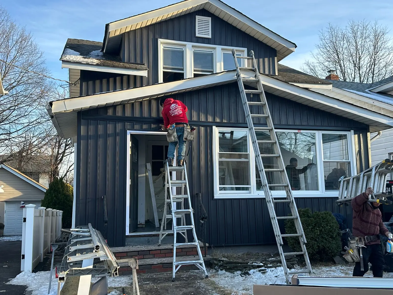 SSKM Construction crew member installing dark vertical siding in winter